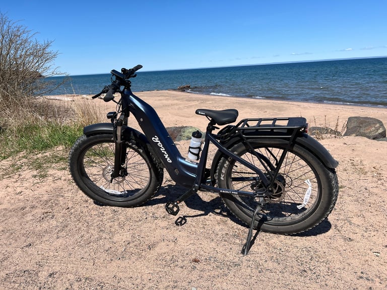 Black electric bike parked on sandy beach with ocean and clear blue sky